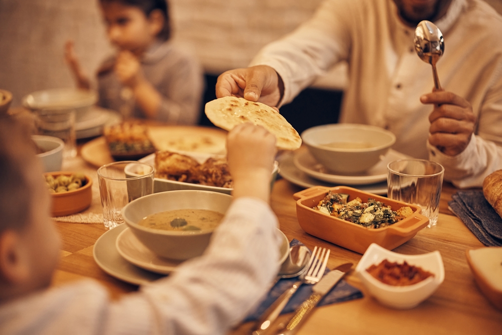 family sitting around the dinner table having a hearty meal in Ramadan, and the father is handing his son bread