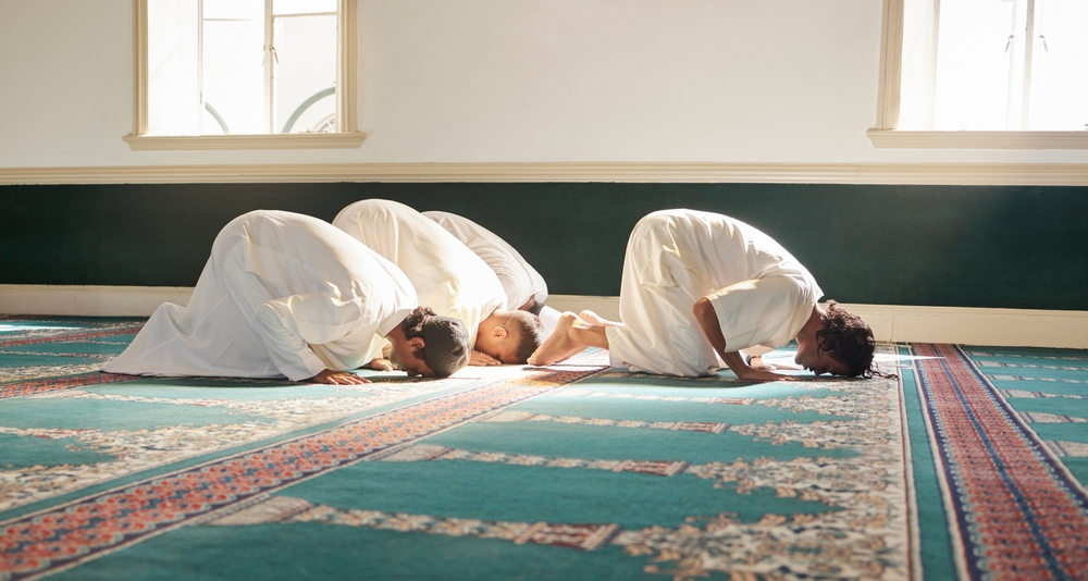 a bunch of men prostrating while praying in a mosque